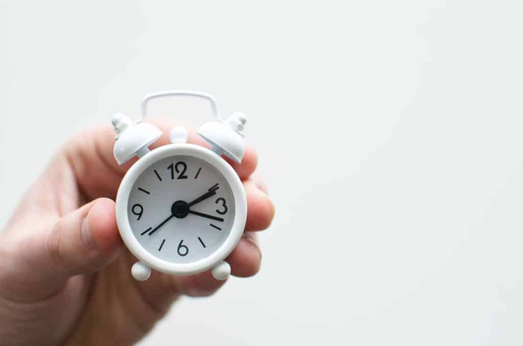 How to set boundaries as a teacher - set a finite time for marking. A hand holding a small alarm clock
