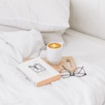 exposing self care myths - photo of a bed with a book, coffee and reading glasses